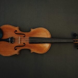 A wooden violin displayed on a dark textured surface, showcasing its craftsmanship.